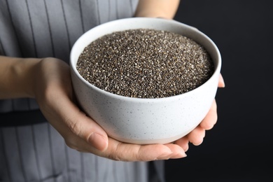 Photo of Woman holding bowl with chia seeds on dark background, closeup