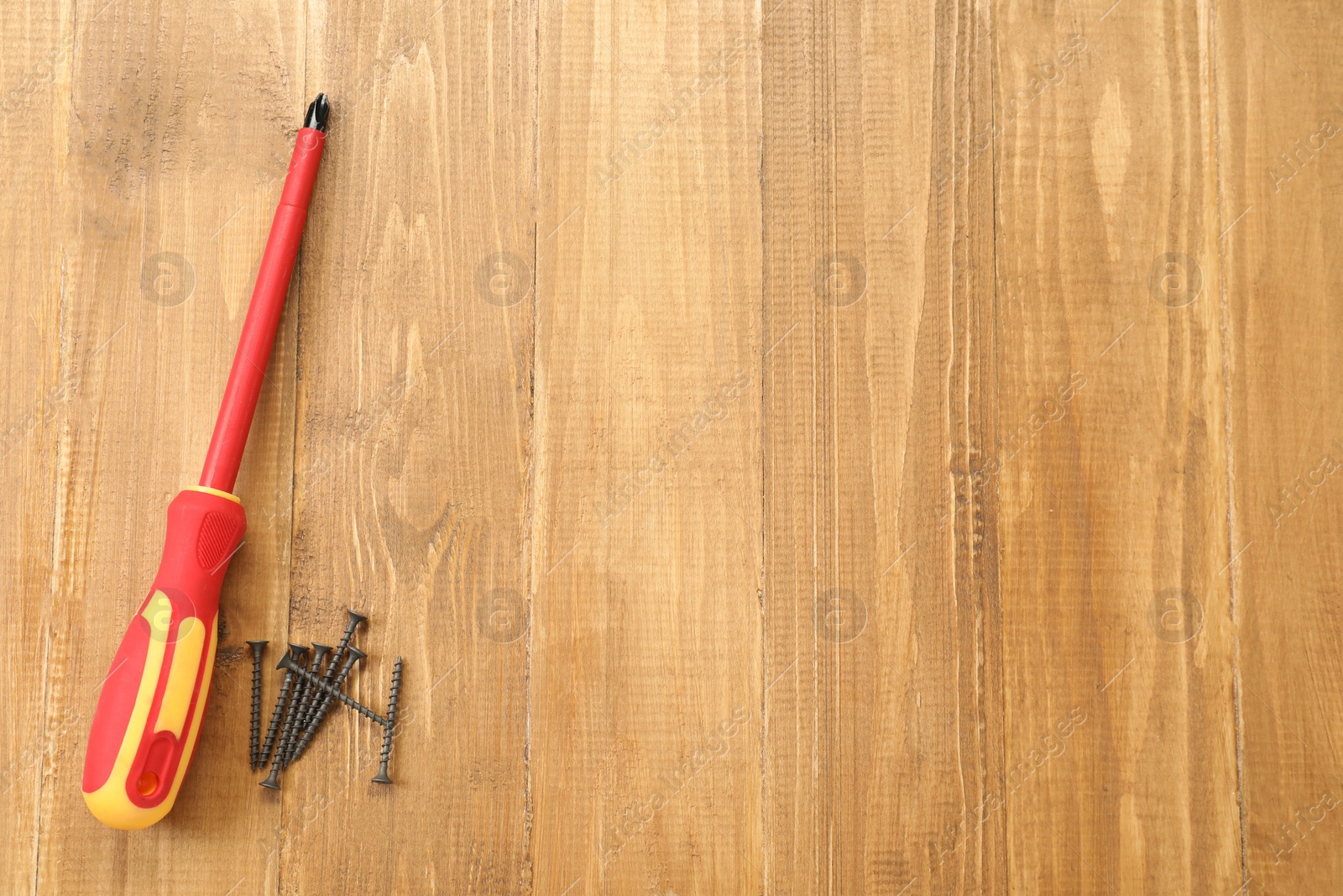 Photo of Screwdriver with red handle and screws on table, flat lay. Space for text