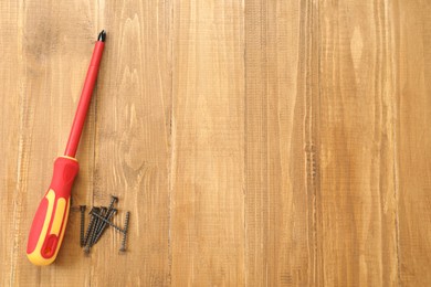 Photo of Screwdriver with red handle and screws on table, flat lay. Space for text