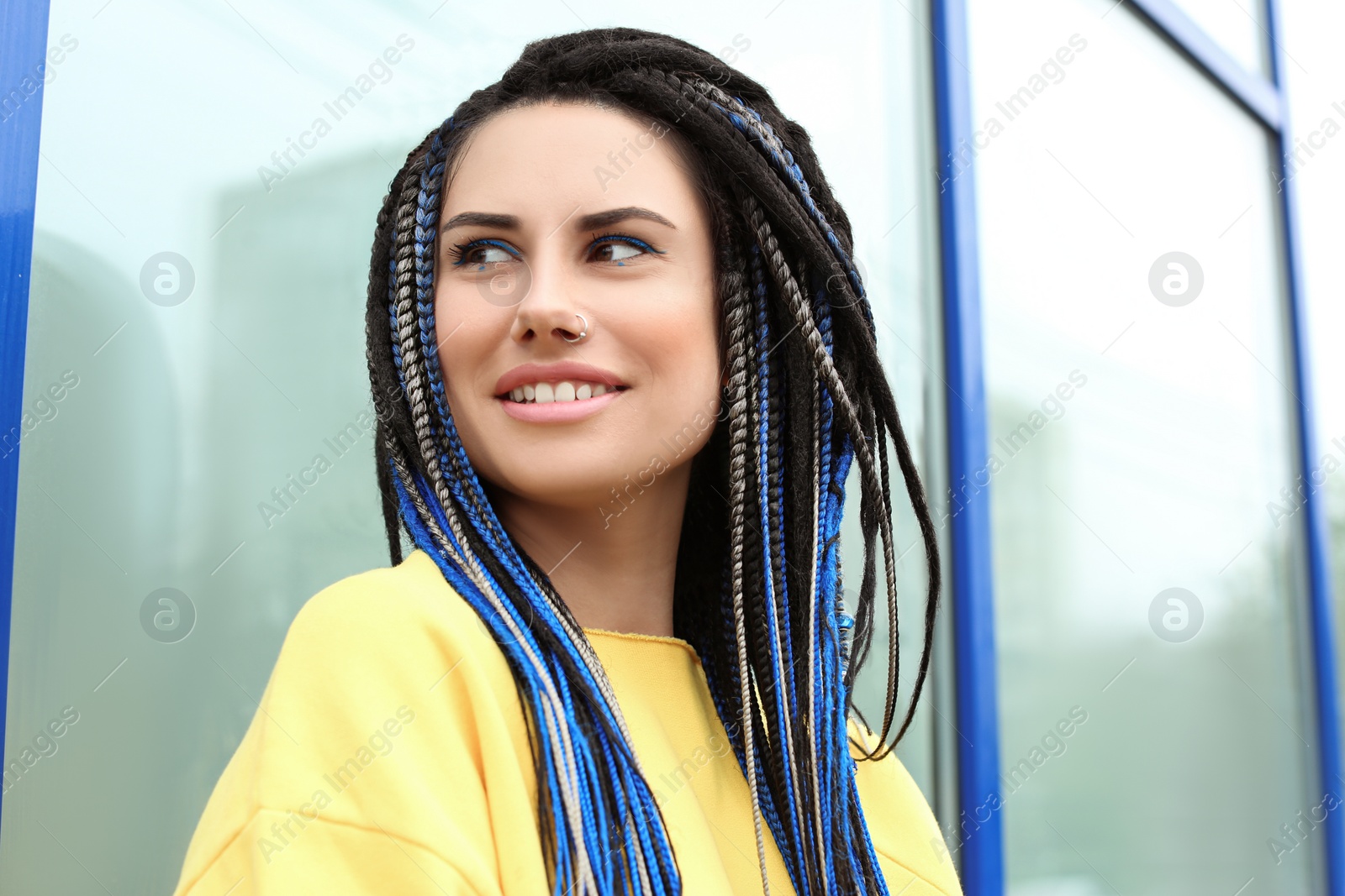 Photo of Beautiful young woman with nose piercing and dreadlocks near wall outdoors