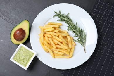 Plate with french fries, guacamole dip, rosemary and avocado served on black table, top view