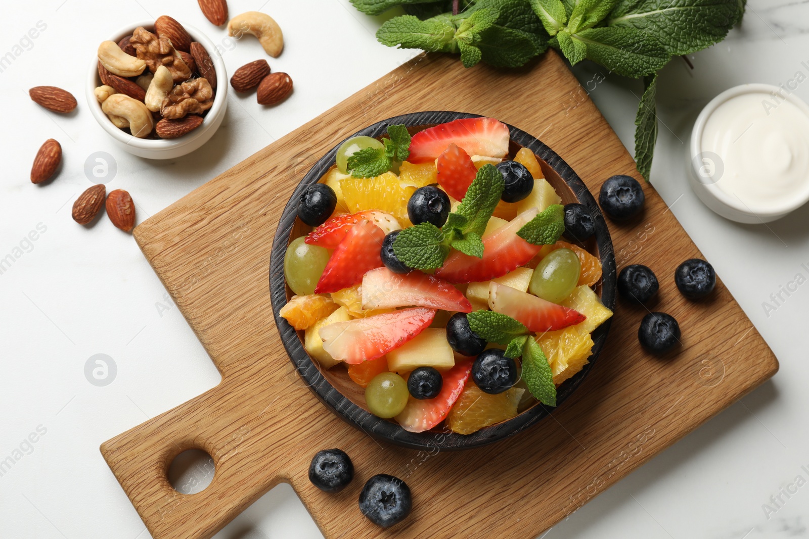 Photo of Delicious fruit salad in bowl, berries, nuts and fresh mint on white table, flat lay