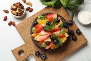 Photo of Delicious fruit salad in bowl, berries, nuts and fresh mint on white table, flat lay