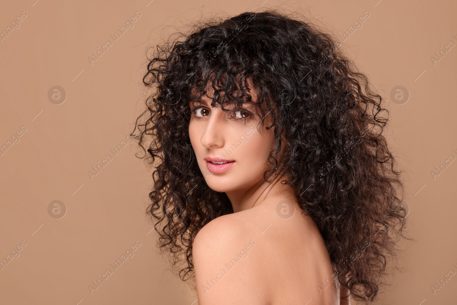 Photo of Beautiful young woman with long curly hair on beige background