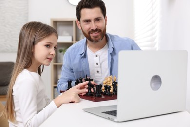 Photo of Father teaching his daughter to play chess following online lesson at home