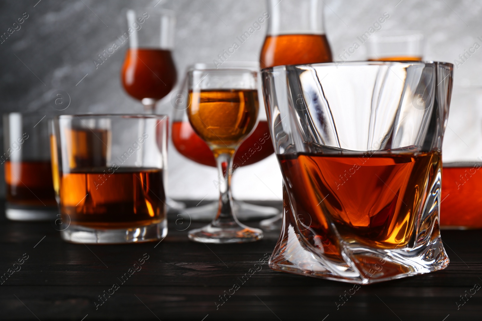 Photo of Different delicious liqueurs in glasses on dark wooden table