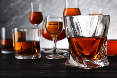 Different delicious liqueurs in glasses on dark wooden table