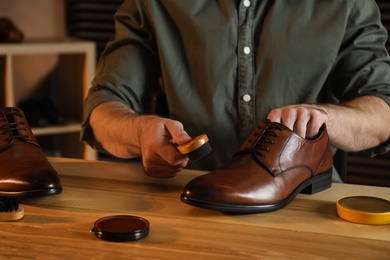 Photo of Man taking professional care of brown leather shoes in workshop, closeup