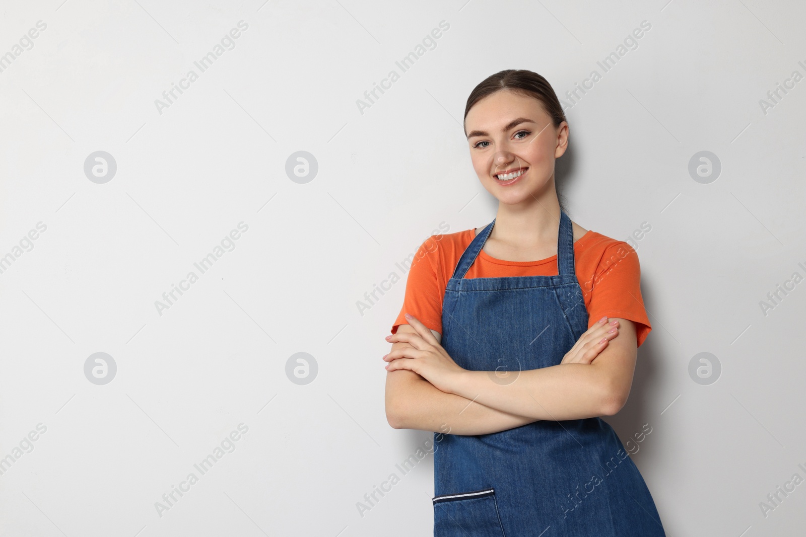 Photo of Beautiful young woman in clean denim apron on light grey background. Space for text