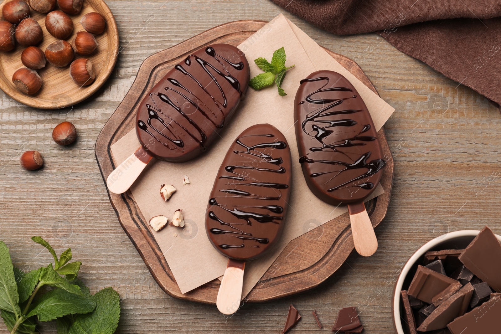 Photo of Delicious glazed ice cream bars, nuts and mint on wooden table, flat lay