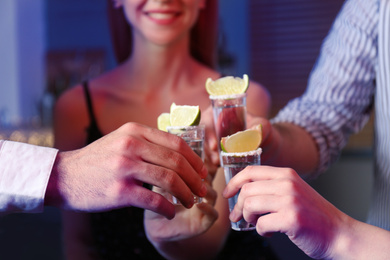 Photo of Young people toasting with Mexican Tequila shots at bar, closeup