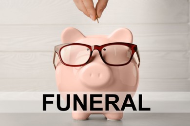 Money for funeral expenses. Woman putting coin into piggy bank at light grey table, closeup