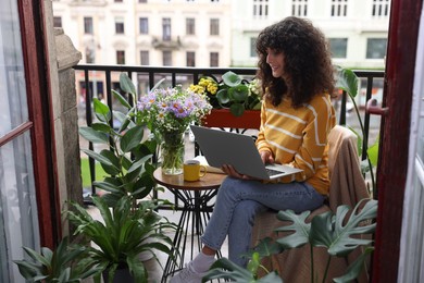 Beautiful young woman using laptop on balcony with green houseplants