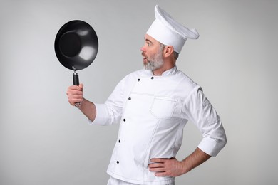 Surprised chef in uniform holding wok on grey background