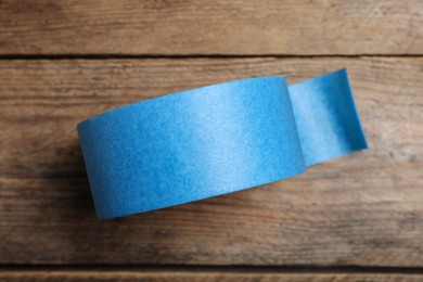 Photo of Roll of light blue adhesive tape on wooden background, top view