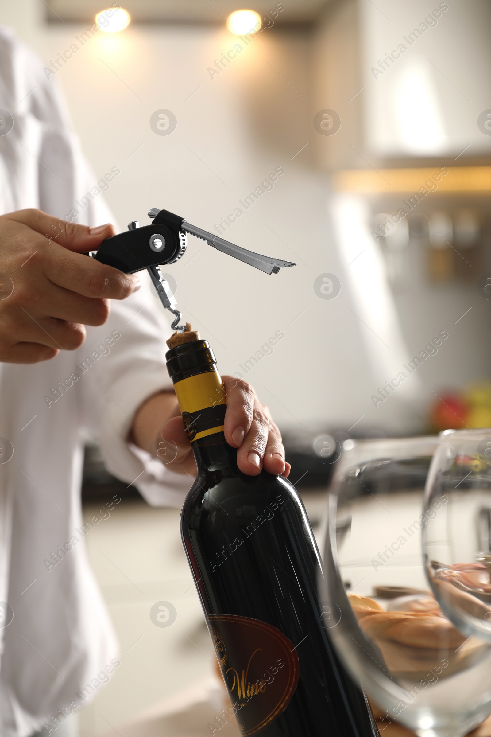 Photo of Woman opening wine bottle with corkscrew at table indoors, closeup