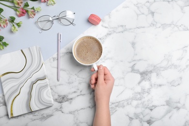 Woman with cup of coffee and stationery at marble table, top view. Space for text