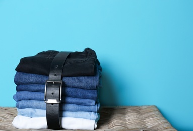 Photo of Stack of different jeans on basket against color wall with space for text