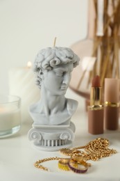 Photo of David bust candle and bijouterie on white table. Stylish decor