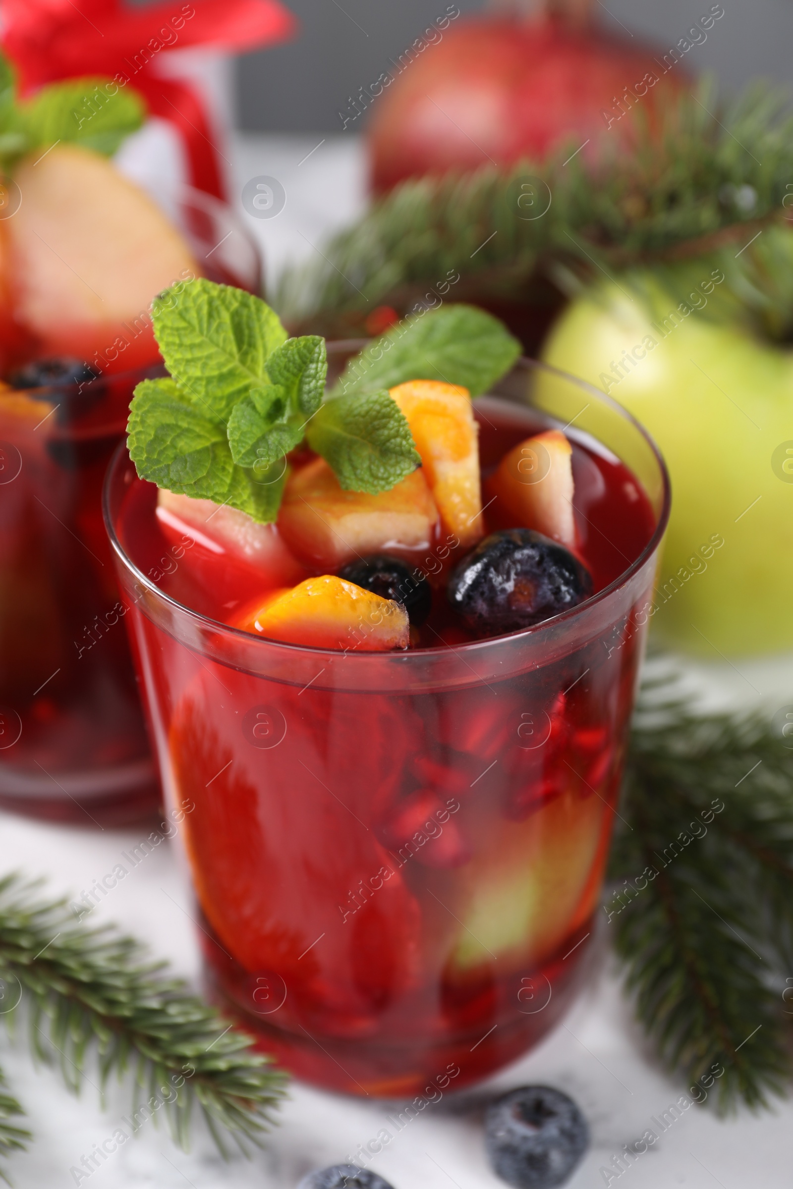 Photo of Aromatic Sangria drink in glass, ingredients and Christmas decor on white marble table