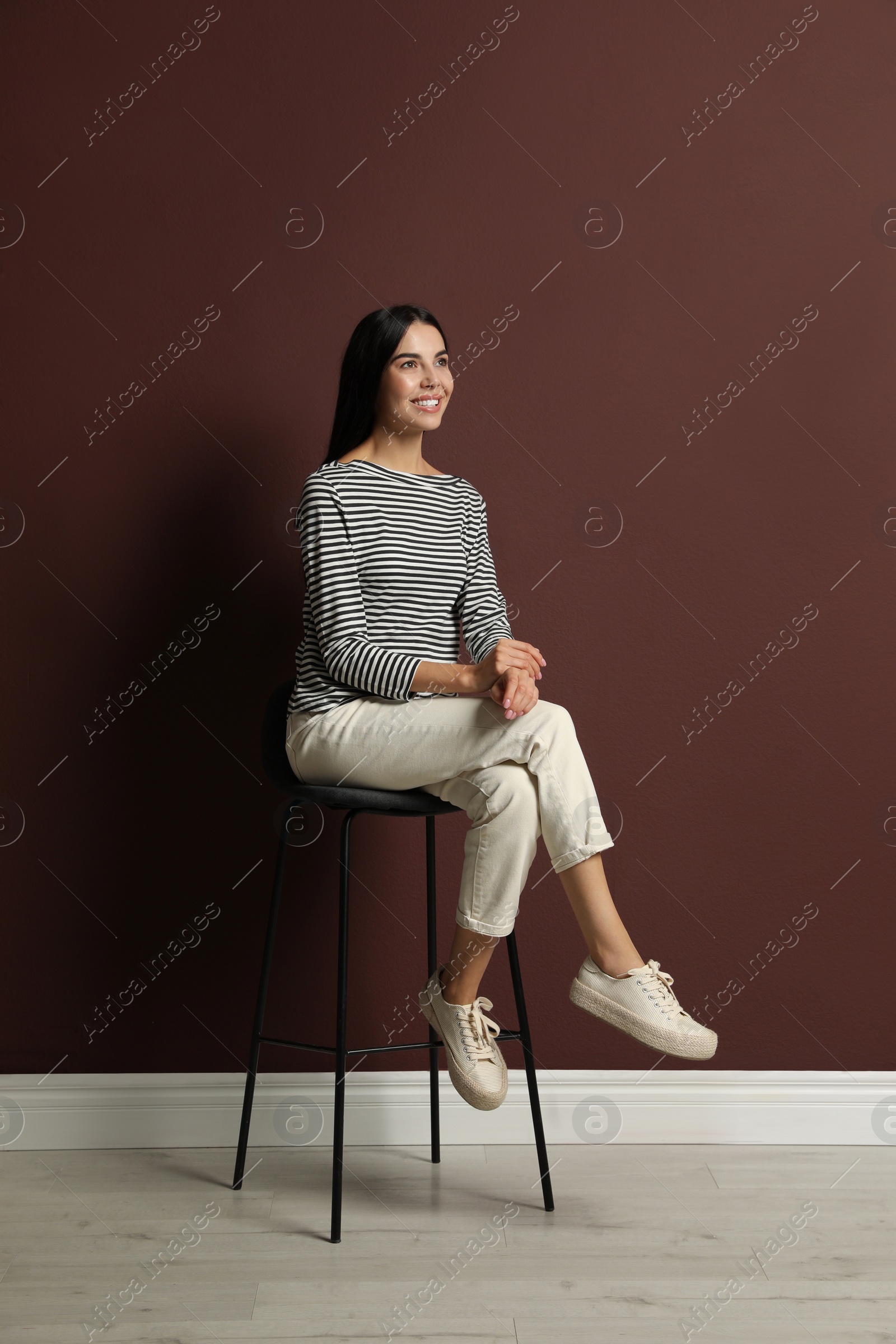 Photo of Beautiful young woman sitting on stool near brown wall