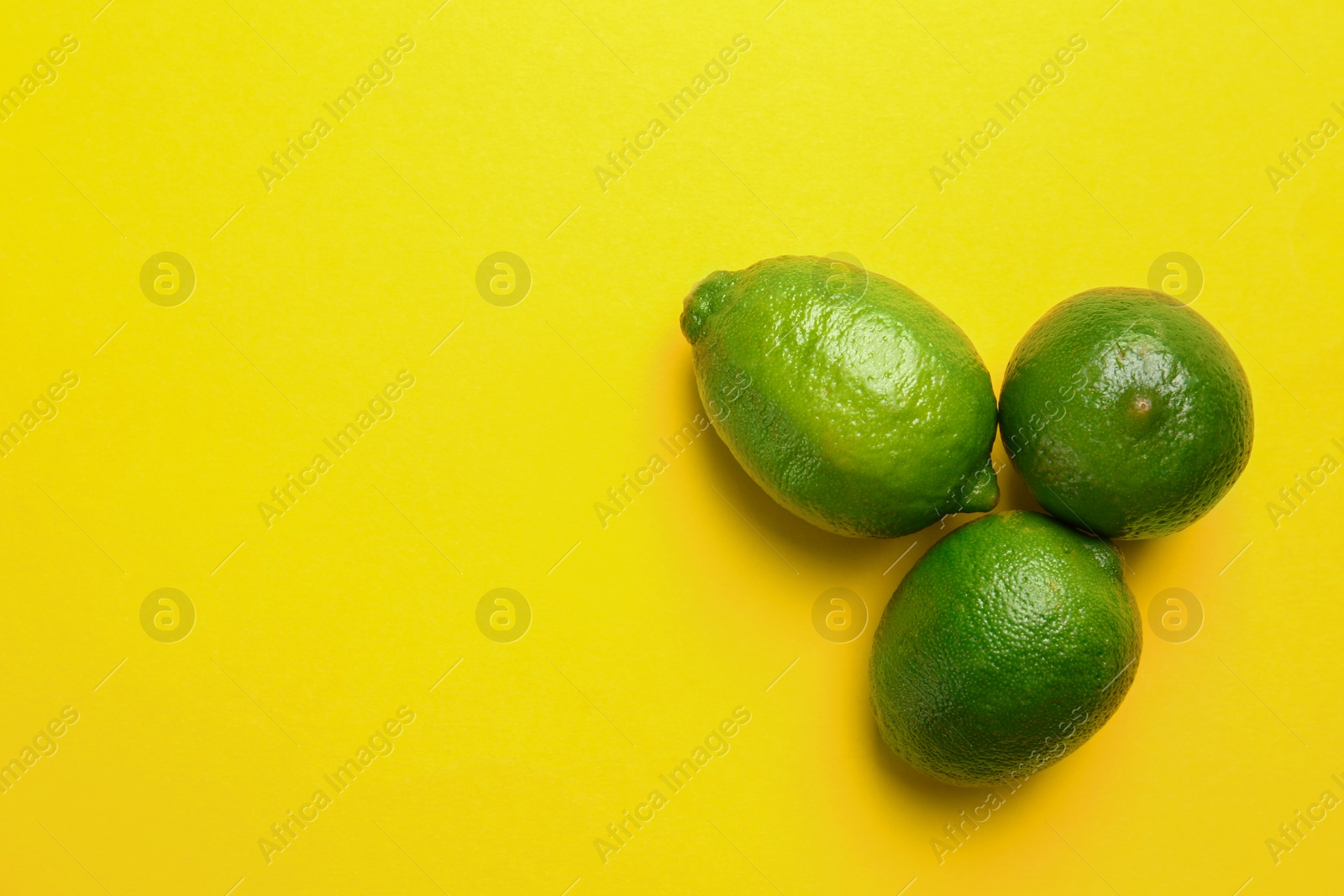 Photo of Ripe tasty limes on yellow background, flat lay with space for text