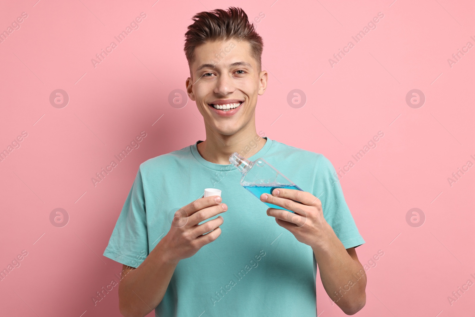 Photo of Young man using mouthwash on pink background