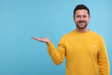 Photo of Special promotion. Smiling man holding something on light blue background. Space for text