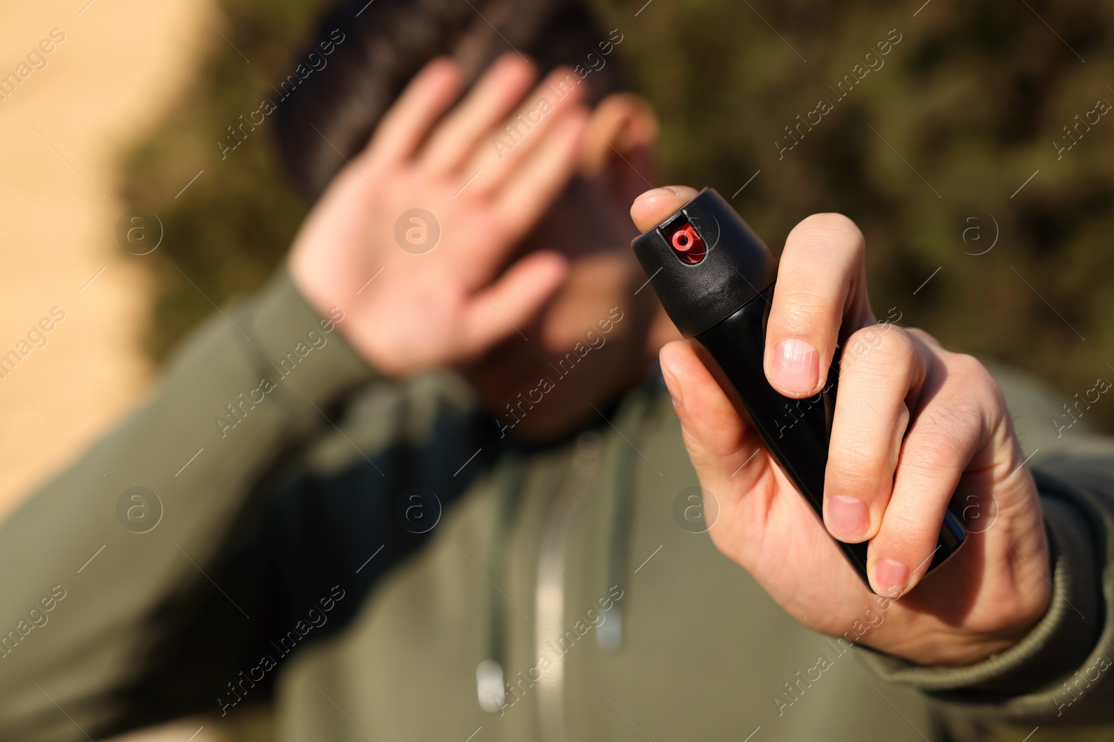 Photo of Man covering eyes with hand and using pepper spray outdoors, focus on canister