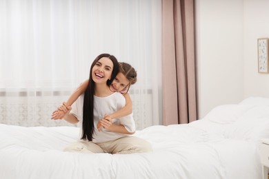 Happy woman and her daughter spending time together on bed at home, space for text. Mother's day celebration
