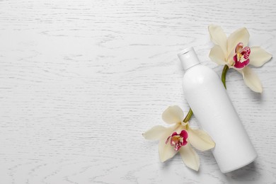 Photo of Bottle of shampoo and flowers on white wooden table, flat lay. Space for text