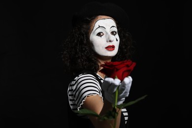 Photo of Young woman in mime costume with red rose posing on black background