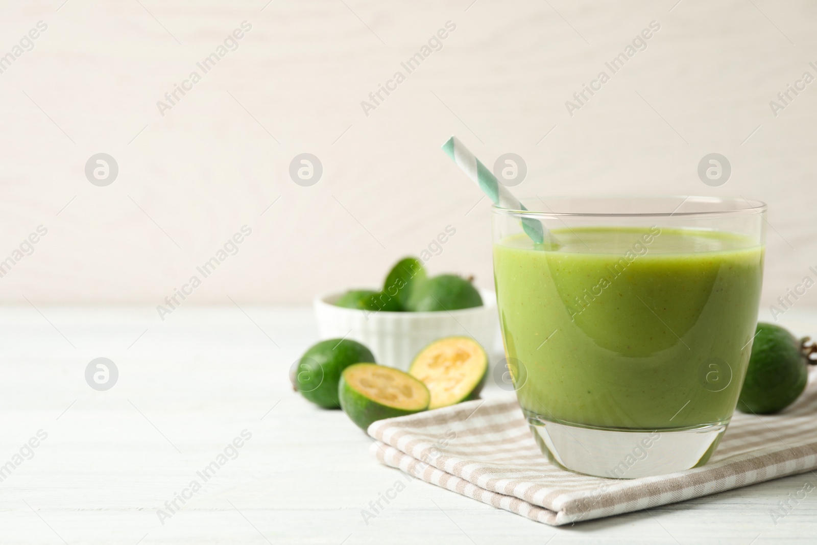 Photo of Fresh feijoa smoothie in glass on white wooden table, closeup. Space for text