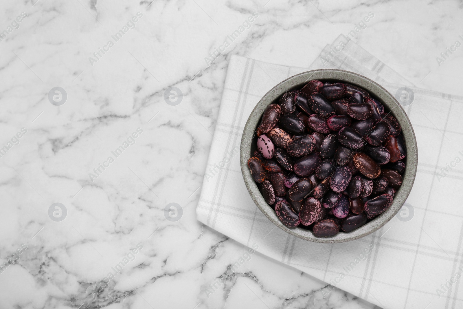 Photo of Bowl with dry kidney beans on white marble table, top view. Space for text