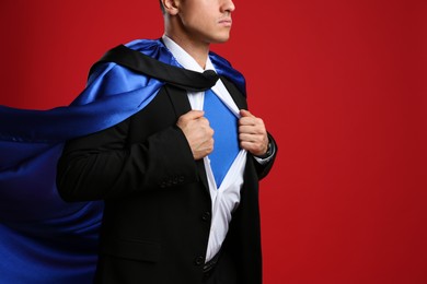 Photo of Businessman in superhero cape taking suit off on red background, closeup
