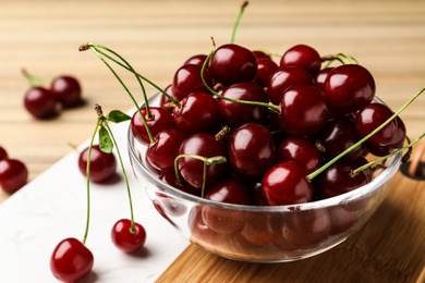 Photo of Glass bowl of delicious cherries on cutting board, closeup view. Space for text