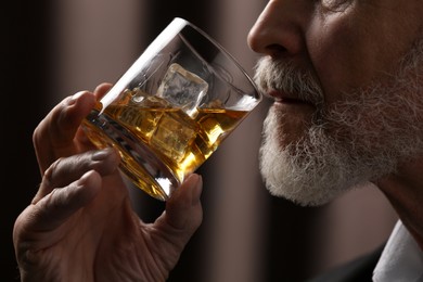 Photo of Senior man drinking whiskey on brown background, closeup