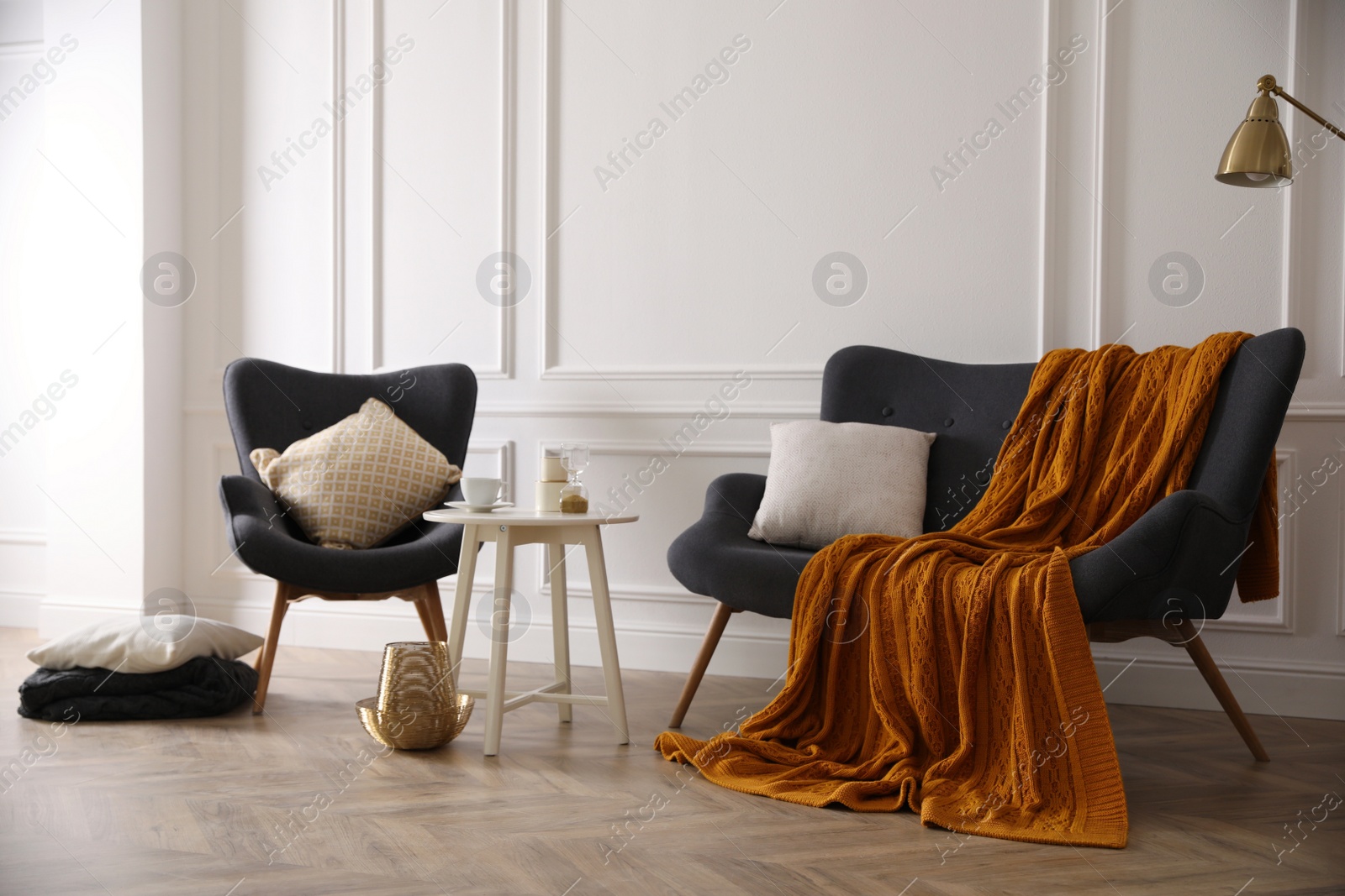 Photo of Comfortable sofa with knitted blanket, armchair and coffee table in stylish room interior