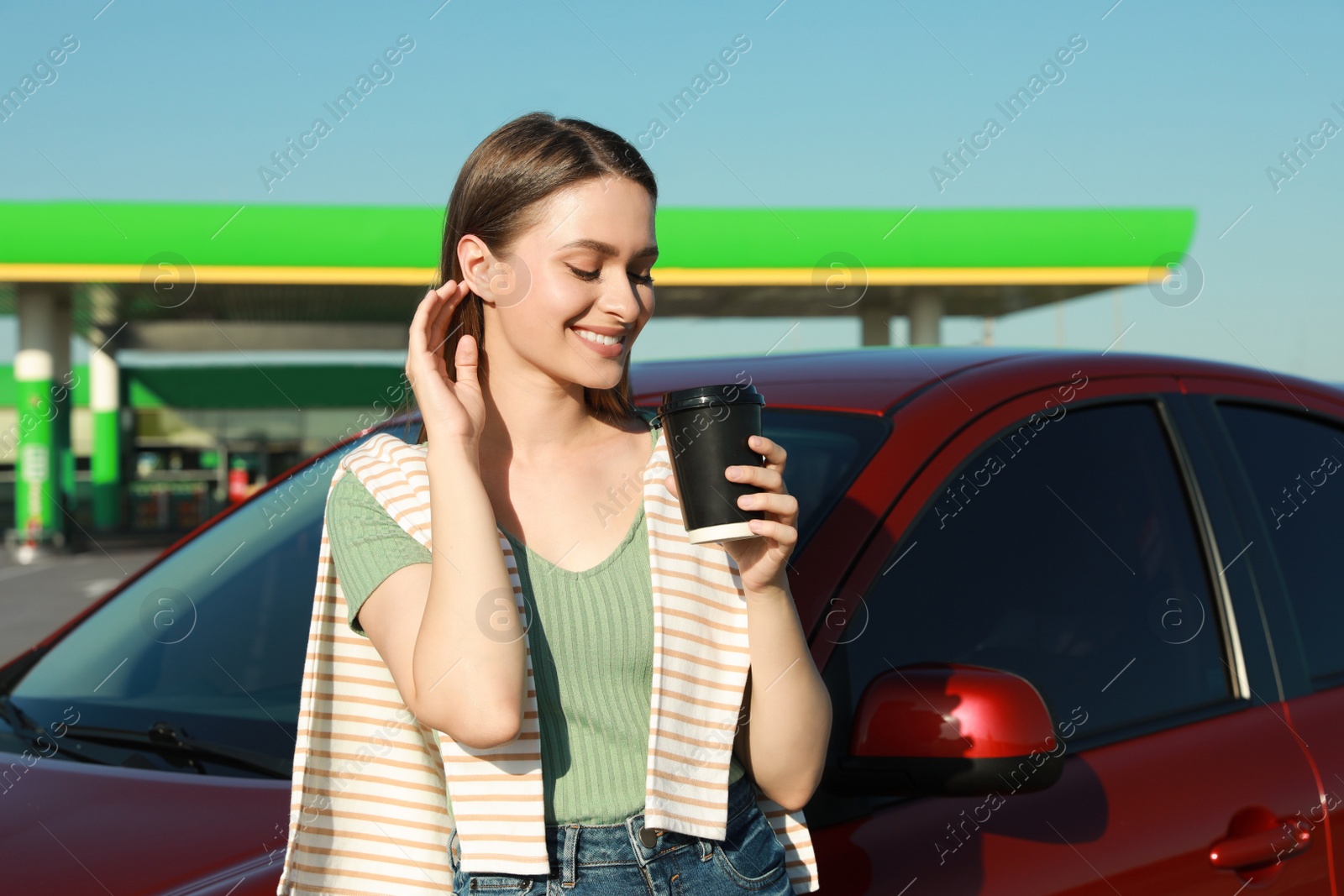 Photo of Beautiful young woman with coffee near car at gas station