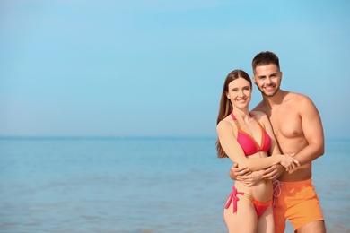 Young woman in bikini with her boyfriend on beach, space for text. Lovely couple