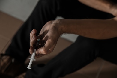 Photo of Young drug addict with syringe sitting on floor, closeup