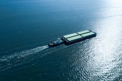 Image of Tugboat pulling barge with cargo by water,  aerial view