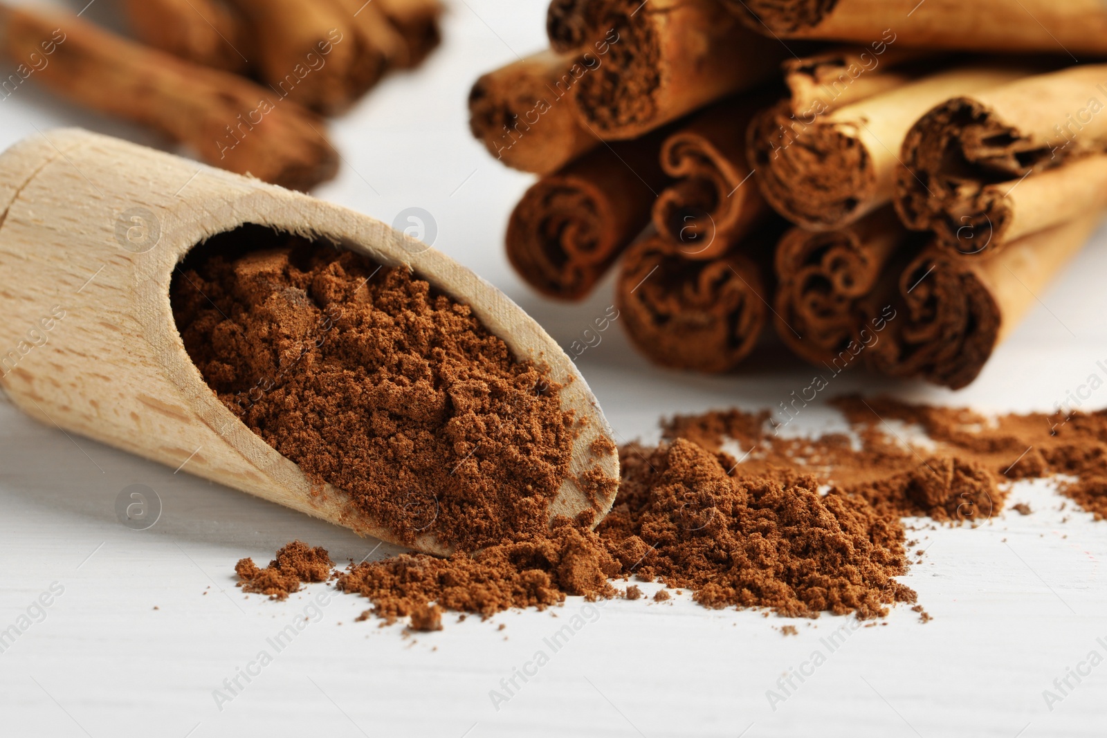 Photo of Scoop with aromatic cinnamon powder and sticks on white table, closeup