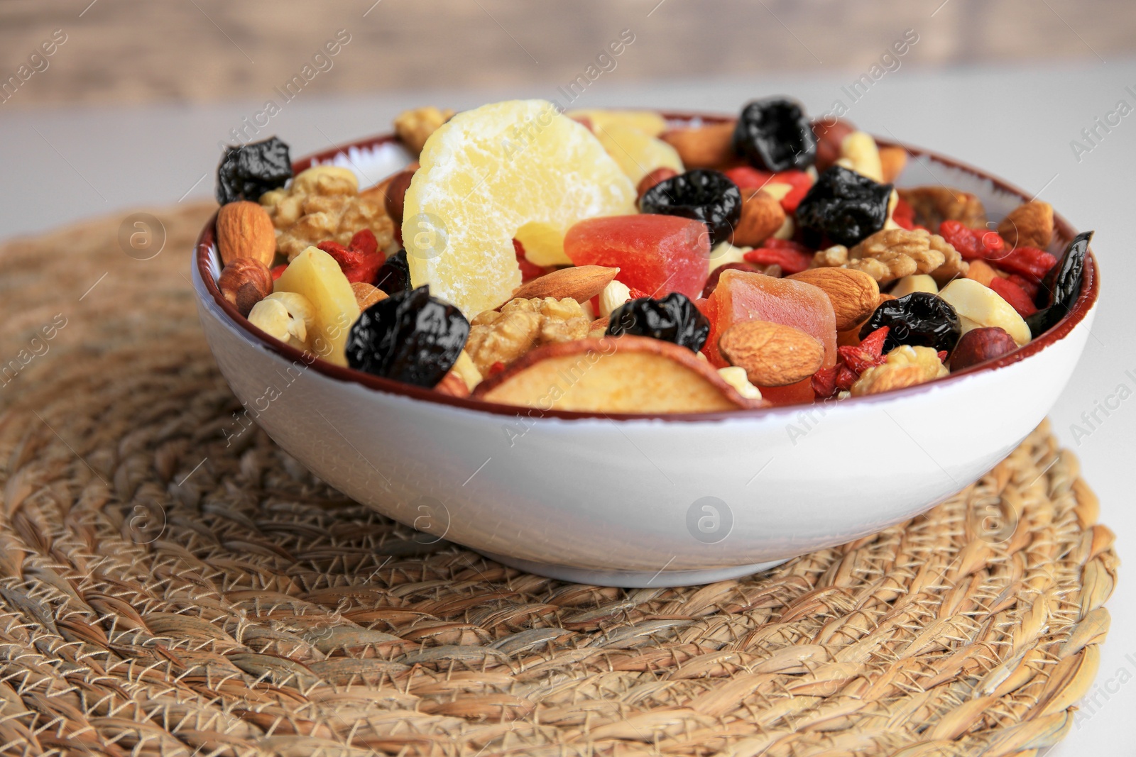 Photo of Bowl with mixed dried fruits and nuts on wicker mat, closeup