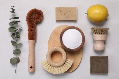 Photo of Cleaning brushes, baking soda, lemon, soap bar and eucalyptus leaves on white table, flat lay