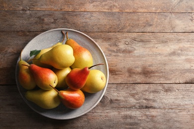 Plate with ripe pears on wooden background, top view. Space for text