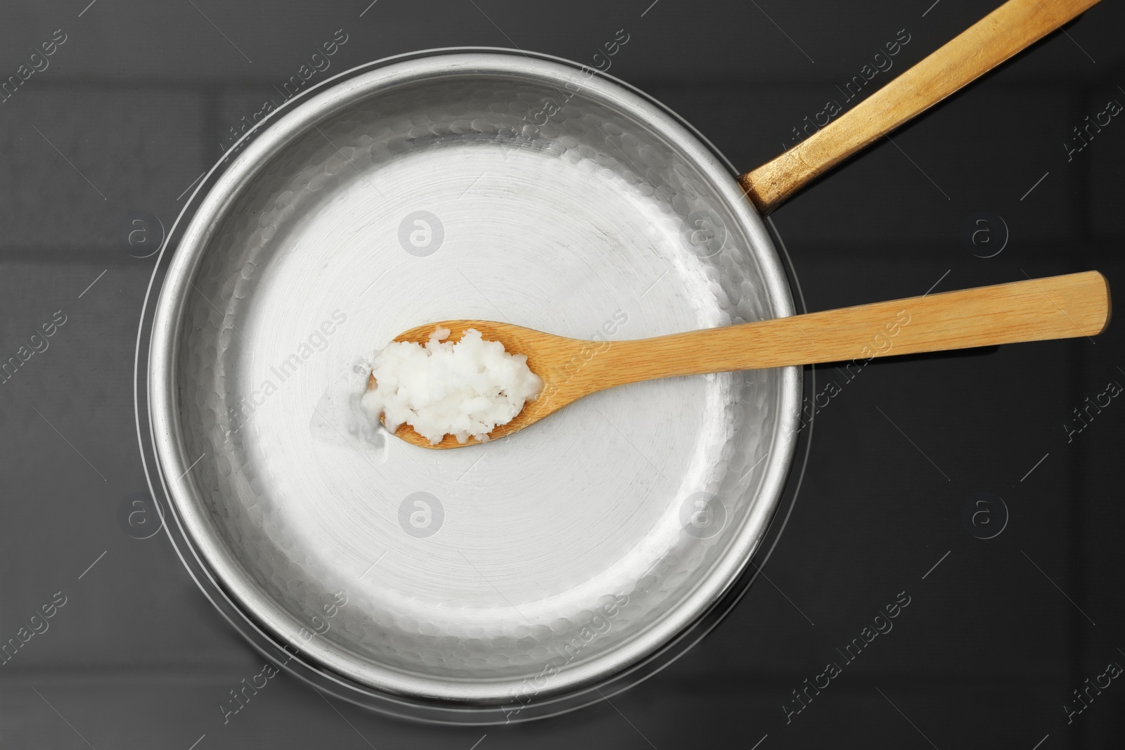 Photo of Frying pan with coconut oil and wooden spatula on induction stove, top view. Healthy cooking