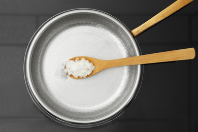 Photo of Frying pan with coconut oil and wooden spatula on induction stove, top view. Healthy cooking