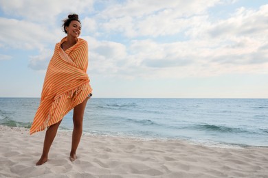 Beautiful African American woman with beach towel on seashore