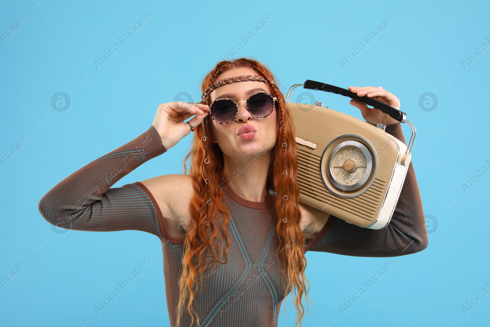 Photo of Stylish young hippie woman with retro radio receiver sending air kiss on light blue background